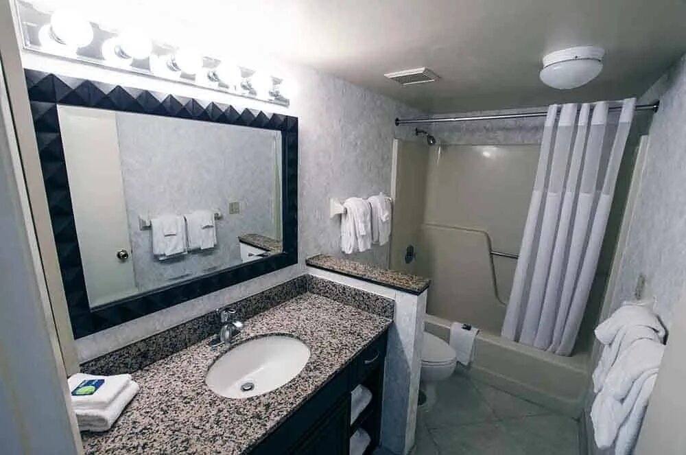 Villa bathroom with a granite vanity, large mirror and tub with shower